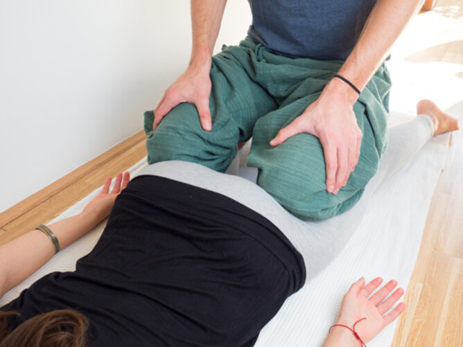 Yoga Kobra Partnerübung | © SONNENTOR Auf dem Foto sieht man wie ein Mann für die Yogaposition die Kobra auf den Hinterbeinen einer Frau kniet. | © SONNENTOR